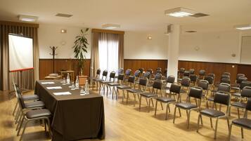 Un salón de conferencias con una mesa larga, sillas y una planta.