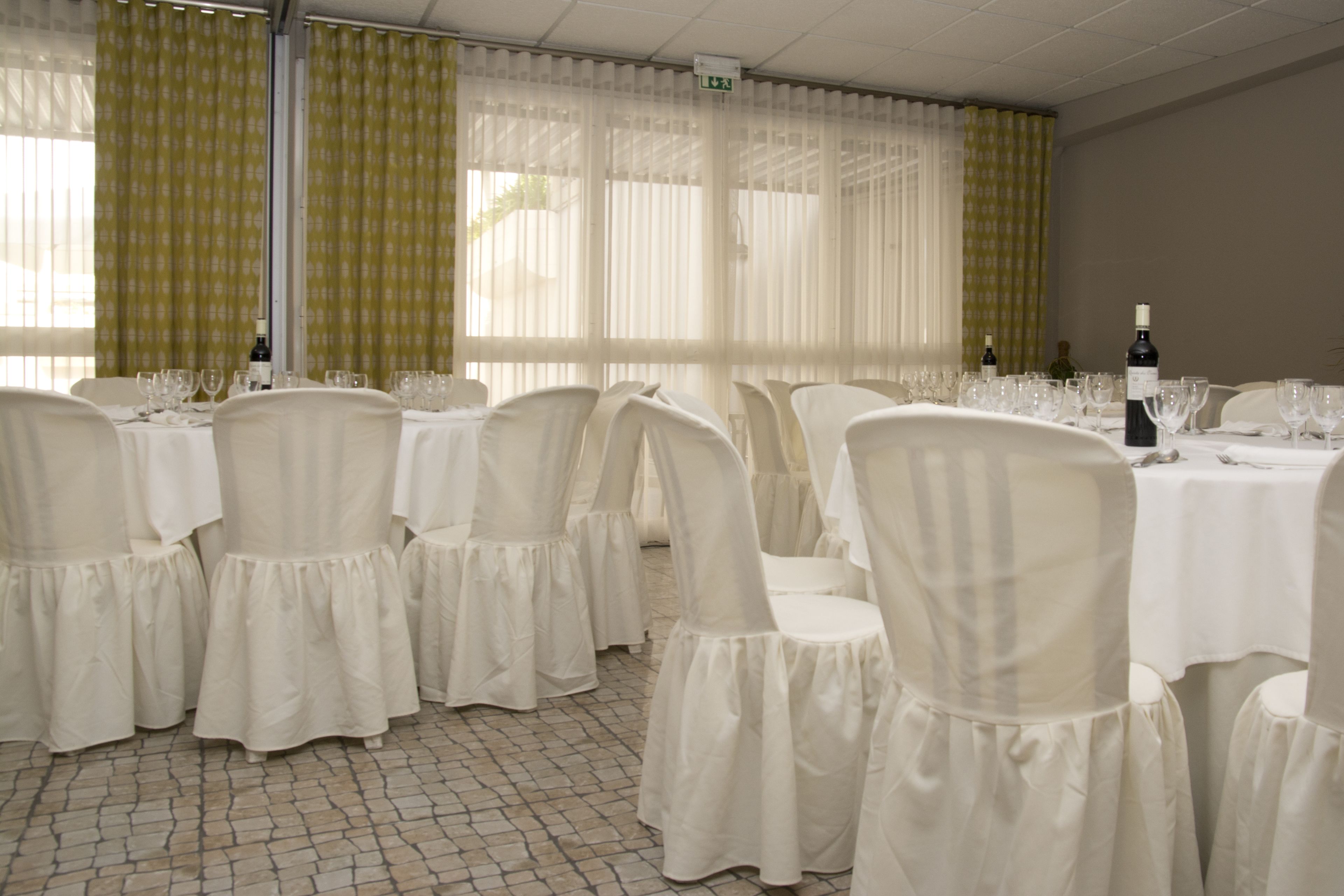Une salle de banquet avec des tables dressées pour le repas, des chaises recouvertes de tissu blanc et des bouteilles de vin posées sur les tables.