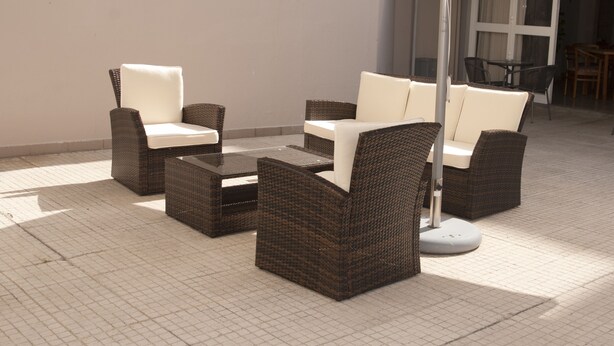 Un patio con mobiliario de mimbre y una mesa de vidrio.