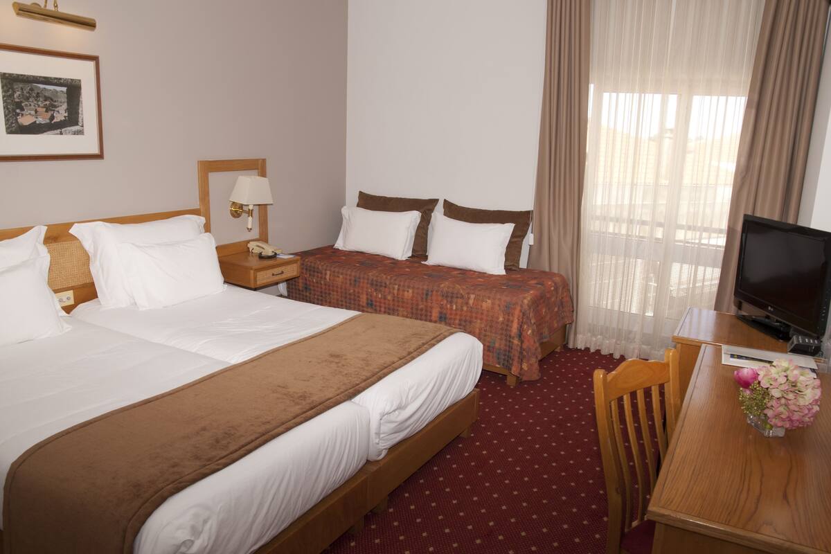 Habitación de hotel con dos camas, un escritorio, una silla, un televisor y una ventana con cortinas.