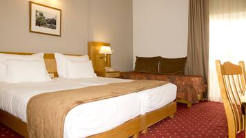 A hotel room with a large bed, a smaller bed, a nightstand with a lamp, a wooden chair, and a framed picture on the wall.