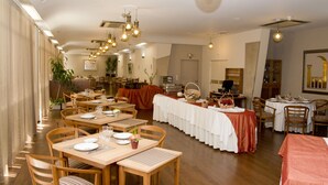 Un comedor amplio con varias mesas dispuestas para comidas, sillas de madera y lámparas colgantes.