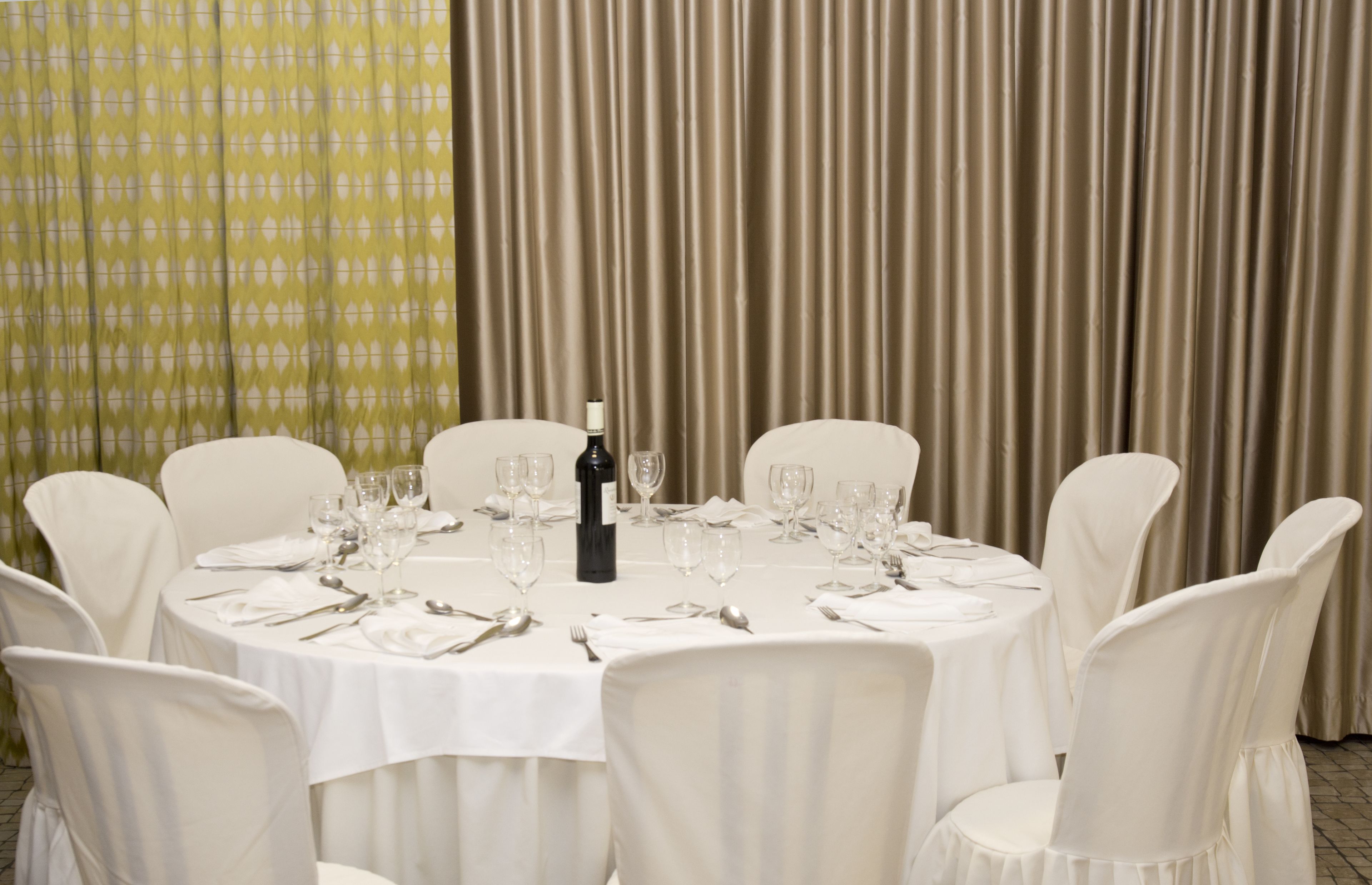 A round dining table set for six with white chairs, a bottle of wine, and multiple wine glasses.