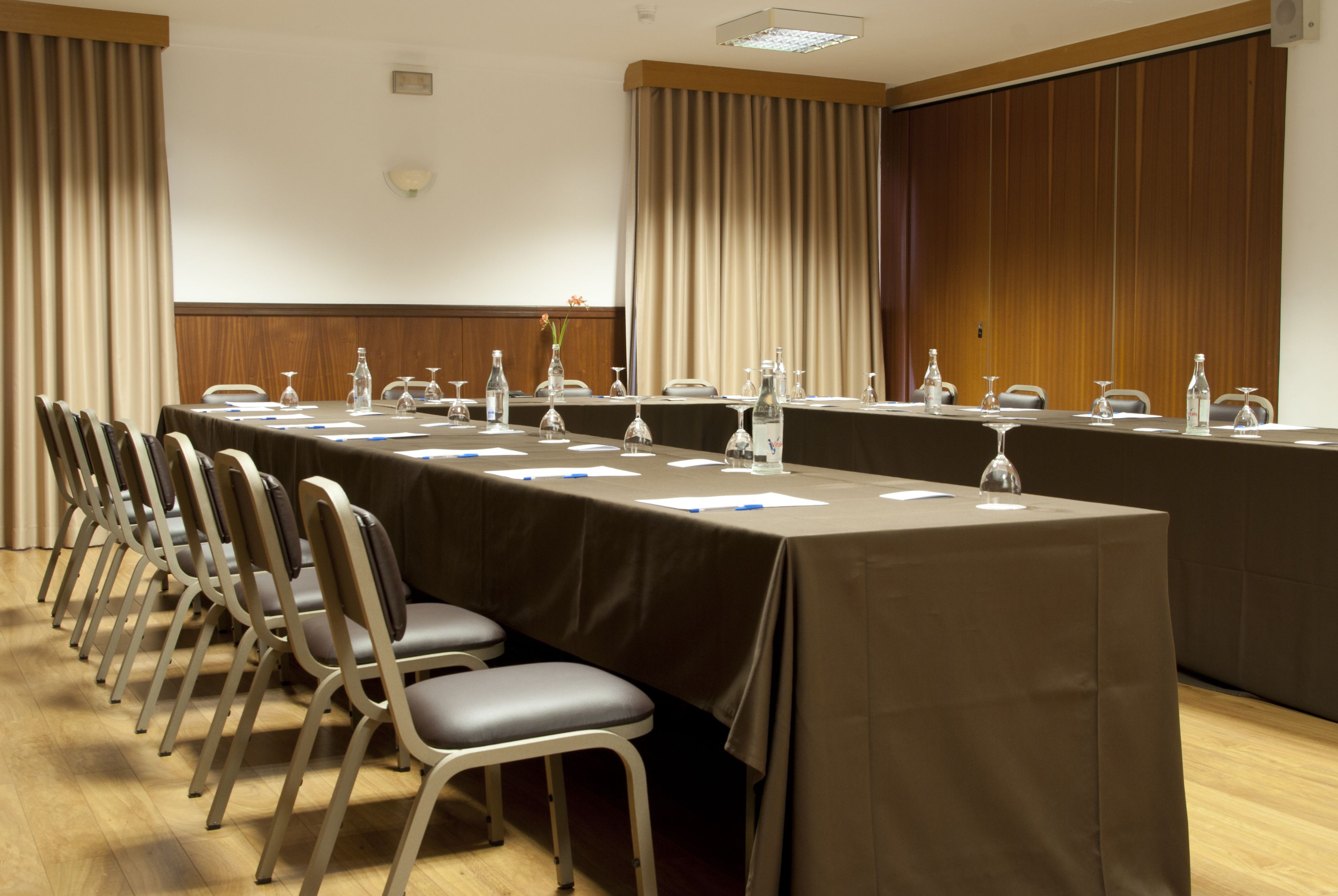 A conference room with a long table, chairs, and a wooden panel wall.
