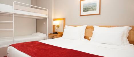 A hotel room with a bunk bed, a single bed, a red throw blanket, a bedside lamp, and a framed picture on the wall.