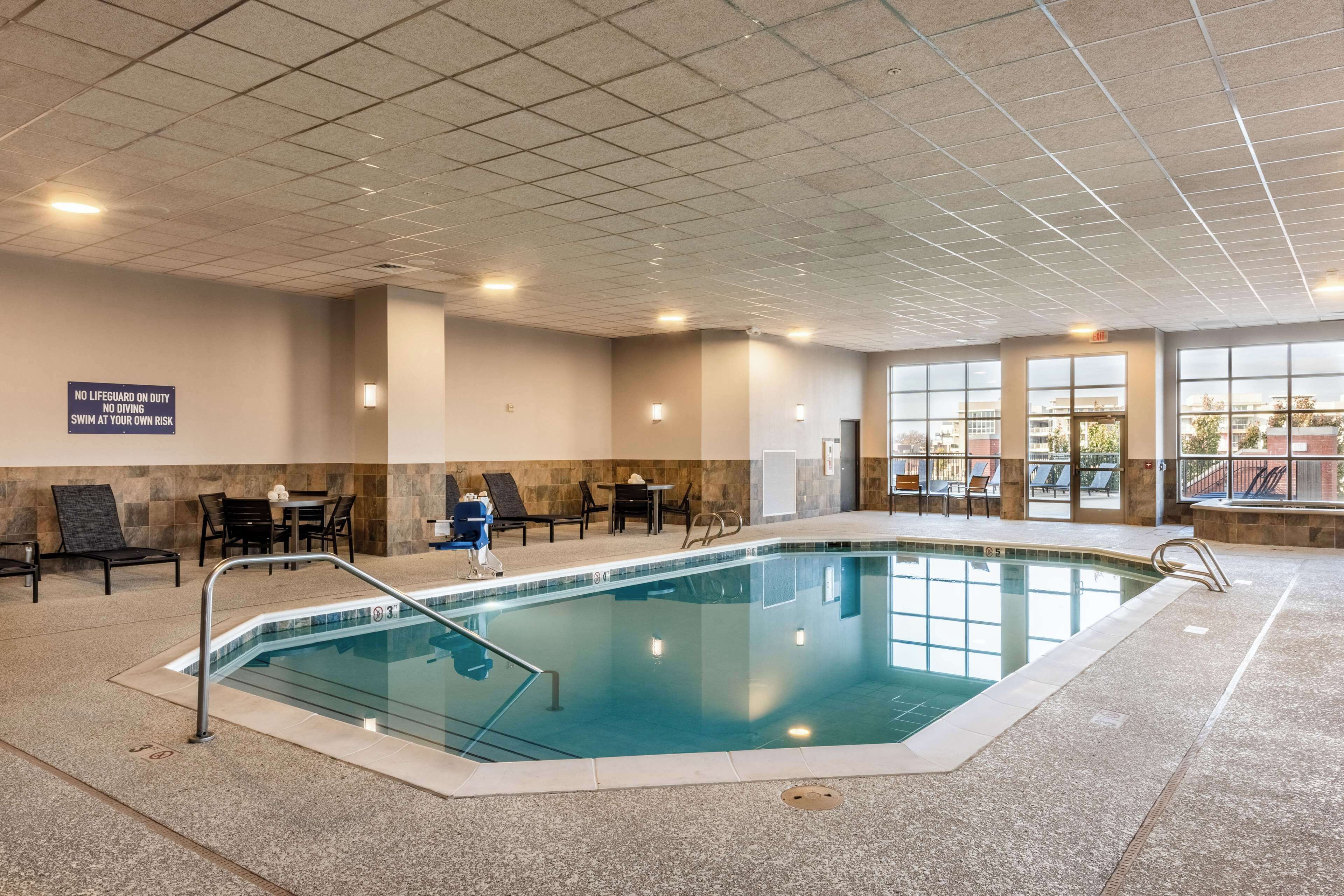An indoor swimming pool with a tiled ceiling, lounge chairs, and a sign warning about swimming risks.
