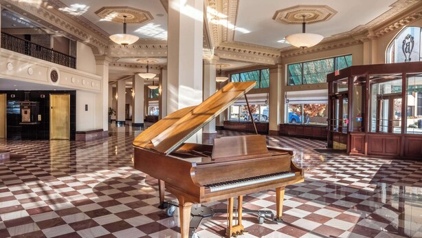 A grand piano in a spacious lobby with a checkered floor, large windows, and classical architectural details. - Drury Plaza Hotel Broadview - Wichita (Wichita)