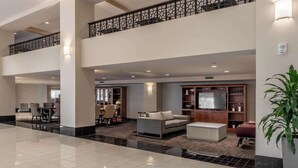 A spacious lobby with a high ceiling, a seating area with a sofa and chairs, a television, and a decorative railing. - Drury Plaza Hotel Broadview - Wichita (Wichita)