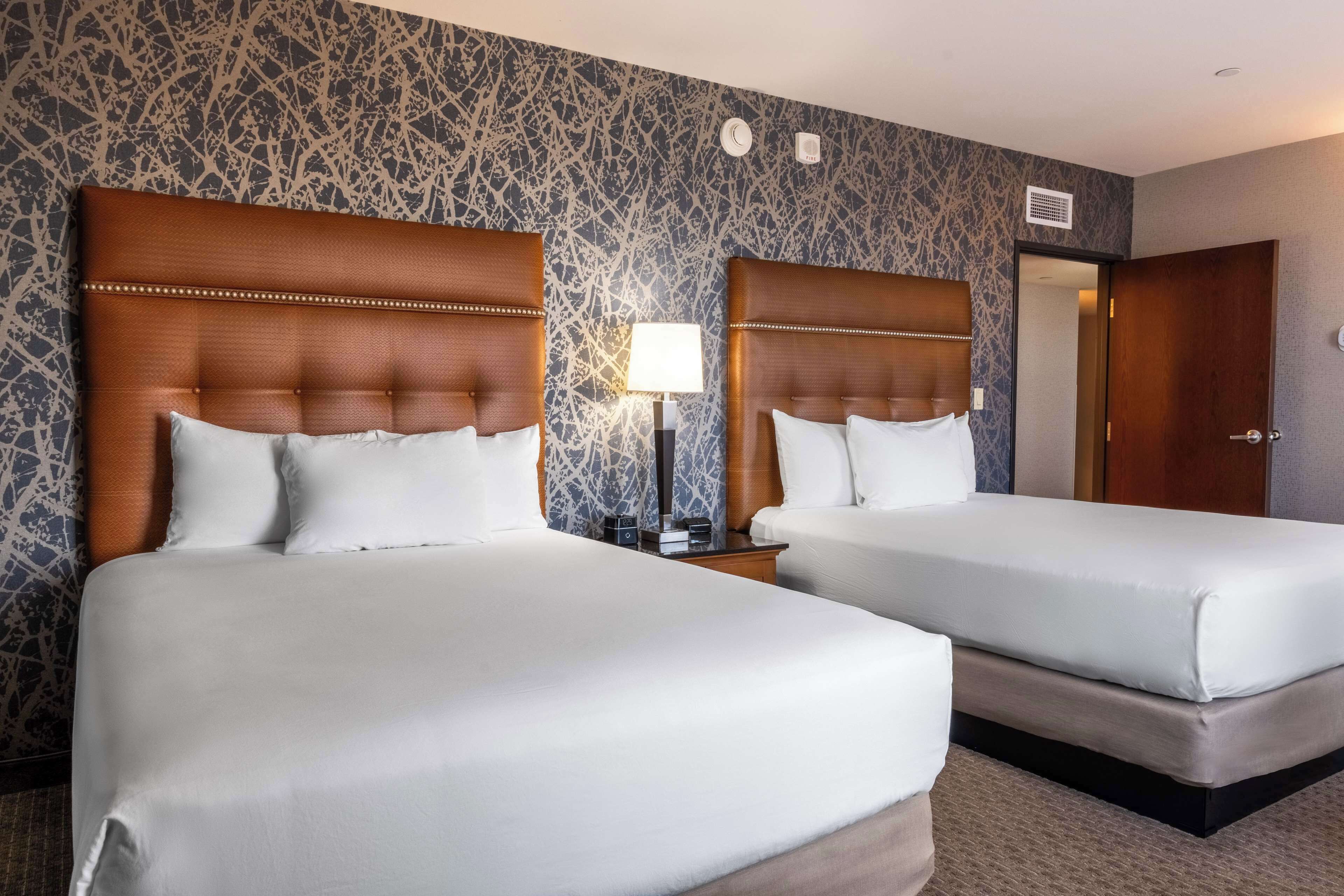 A hotel room with two beds, a nightstand with a lamp, and a patterned wall.
