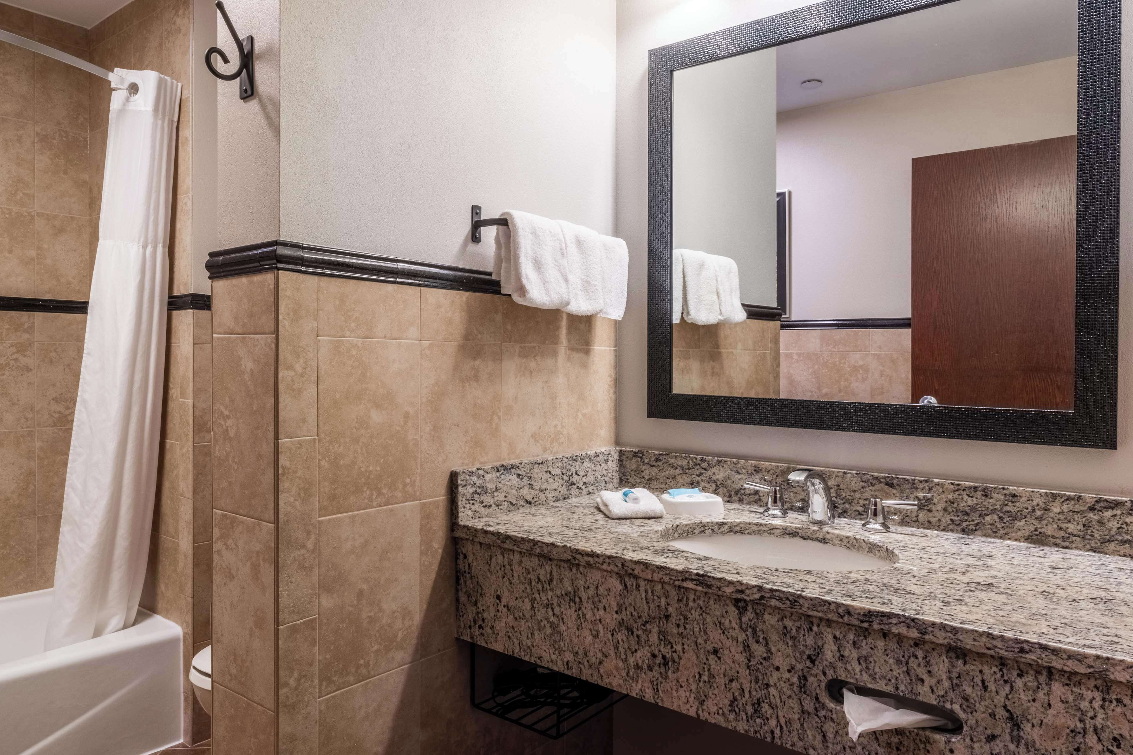 A bathroom with a bathtub, a sink with a granite countertop, a mirror, and a towel rack.