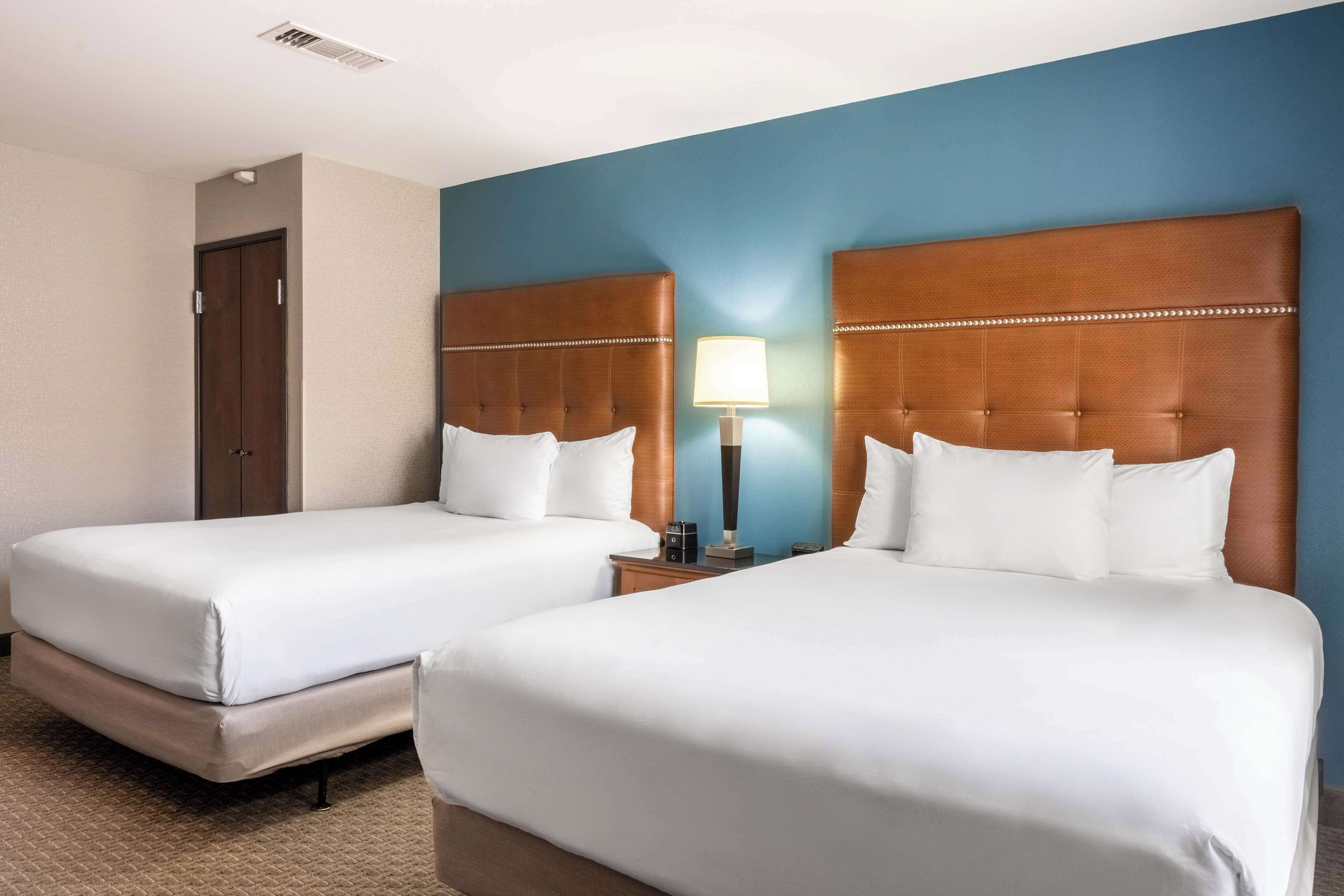 A hotel room with two beds, a nightstand with a lamp, and a door.
