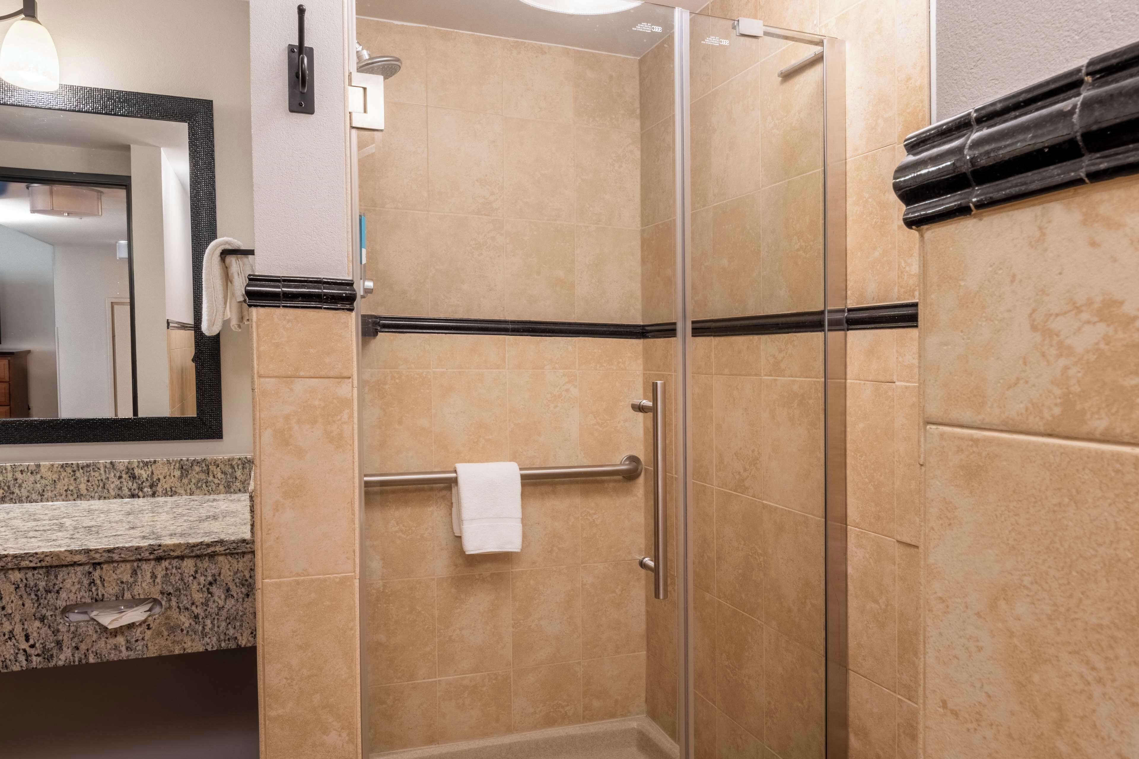 Un bagno moderno con cabina doccia in vetro, piano di lavoro in granito e un ampio specchio.