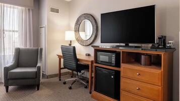 A hotel room with a flat-screen TV, a microwave, a small refrigerator, a desk with a chair, and a large mirror on the wall.