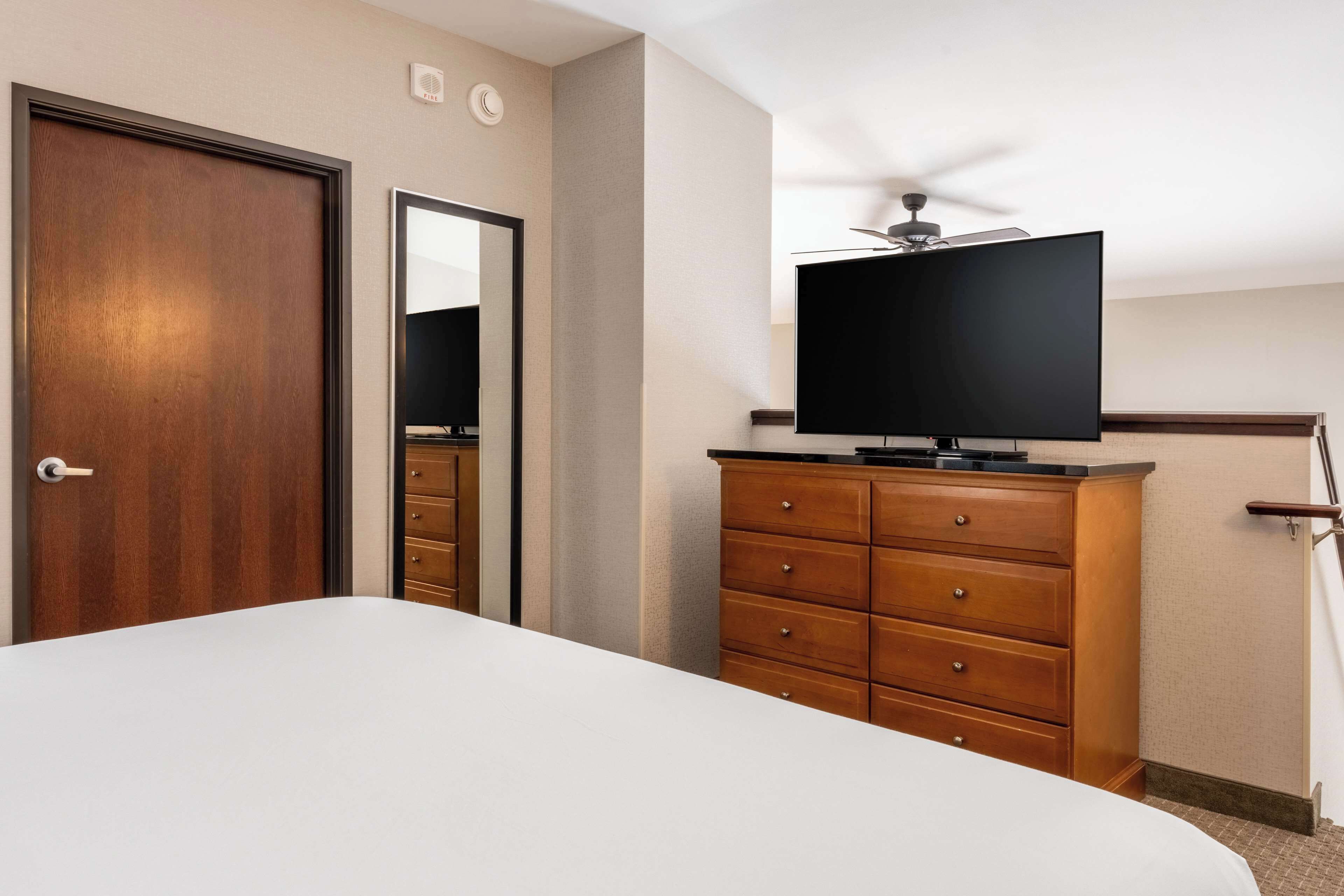 A hotel room with a bed, wooden dresser, television, and ceiling fan.