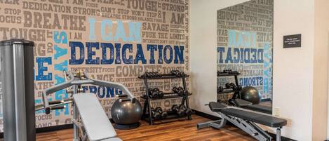 Un gimnasio con equipo de ejercicio, un espejo y frases motivacionales en la pared.