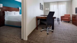A hotel room with a bed, desk, office chair, television, and a view of the outside through curtains. - Sonesta ES Suites Dallas Medical Market Center (Dallas)