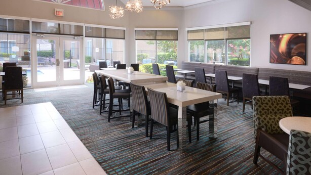 A spacious dining area with multiple tables and chairs, large windows offering views of the outdoors, and a patterned carpet. - Sonesta ES Suites Dallas Medical Market Center (Dallas)