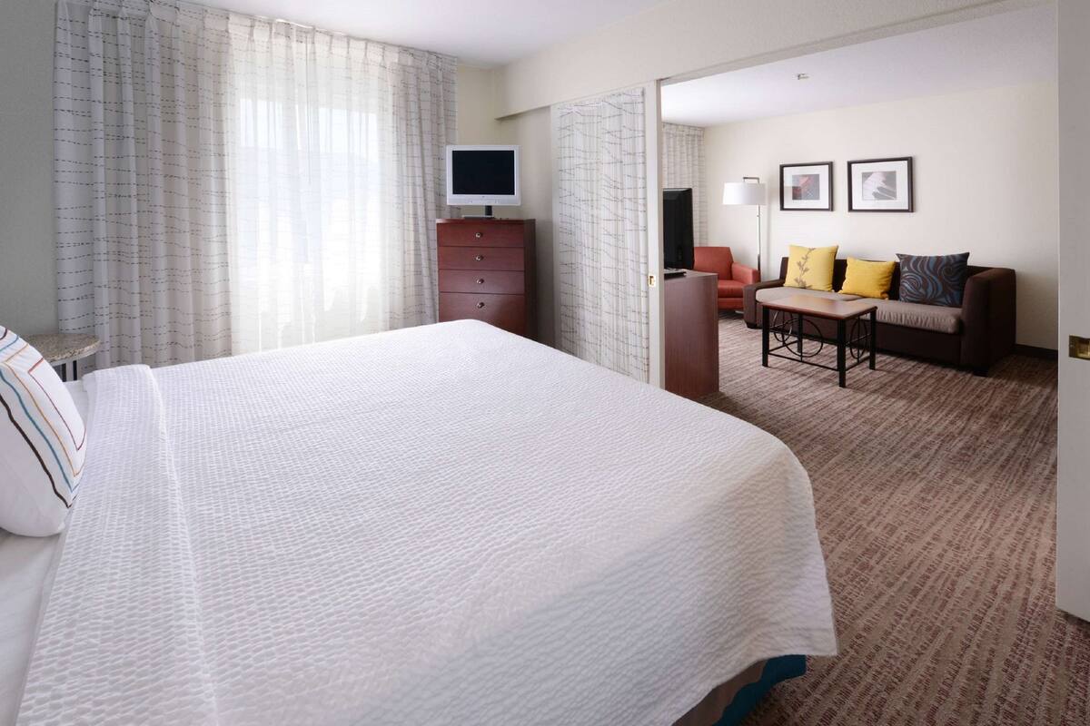 A hotel room with a large bed, a desk, a chair, a television, and a sofa.
