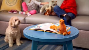 A living room with a round blue table, a sofa, and two children playing with toys.