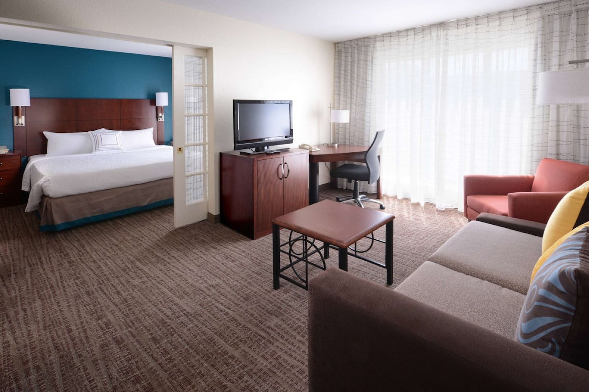 A hotel room with a bed, a desk with a chair, a television, and a sofa.