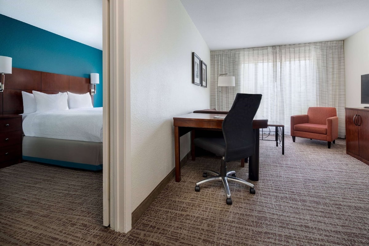 A hotel room with a bed, desk, office chair, and a television.