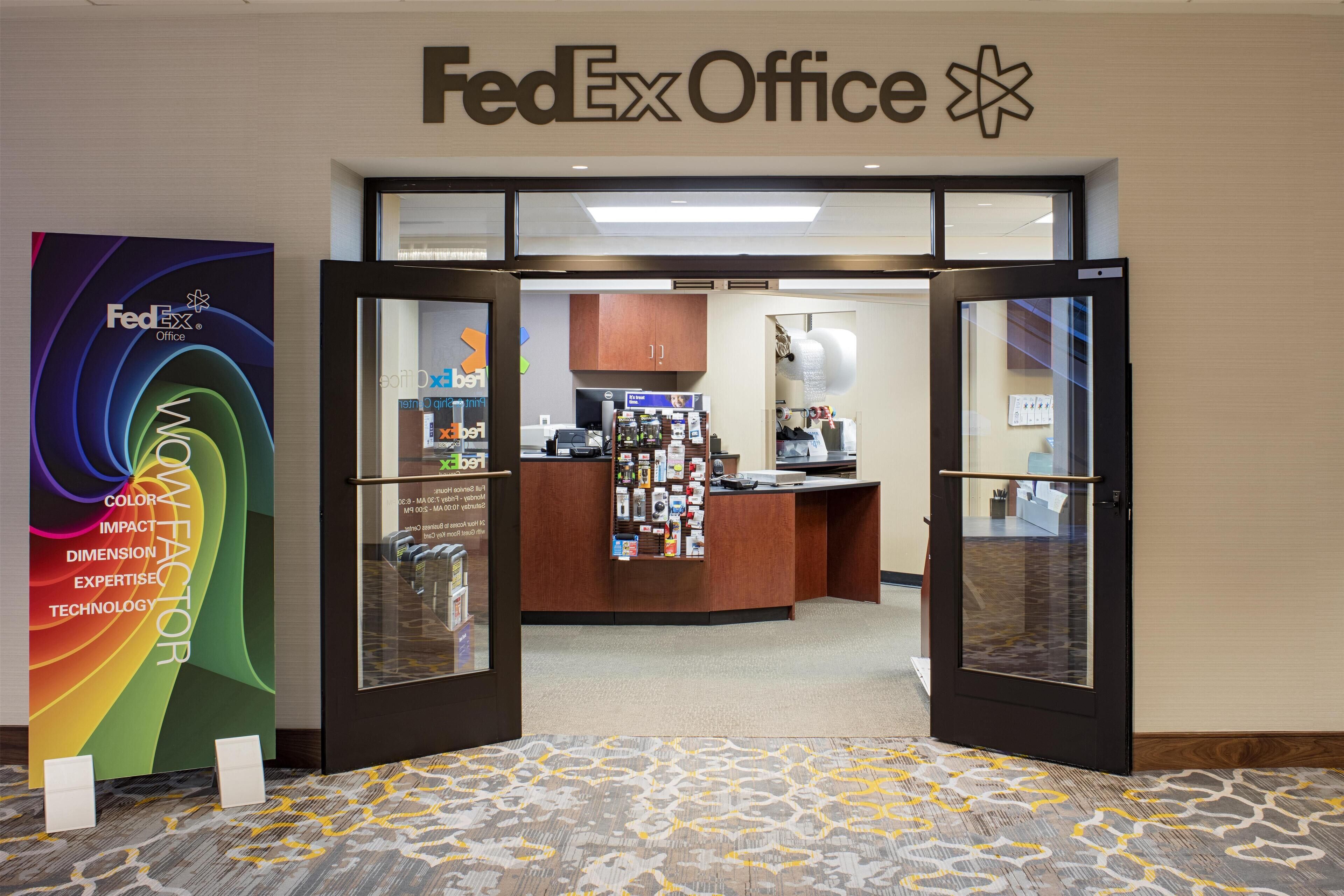 Entrada de uma loja FedEx Office, com balcão de atendimento, mural de avisos e balcão com diversos itens.