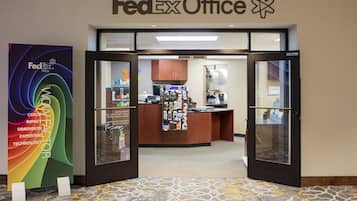 Entrada de uma loja FedEx Office, com balcão de atendimento, mural de avisos e balcão com diversos itens.