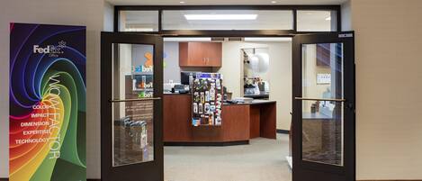 The entrance to a FedEx Office with a reception desk, a bulletin board, and a counter with various items.