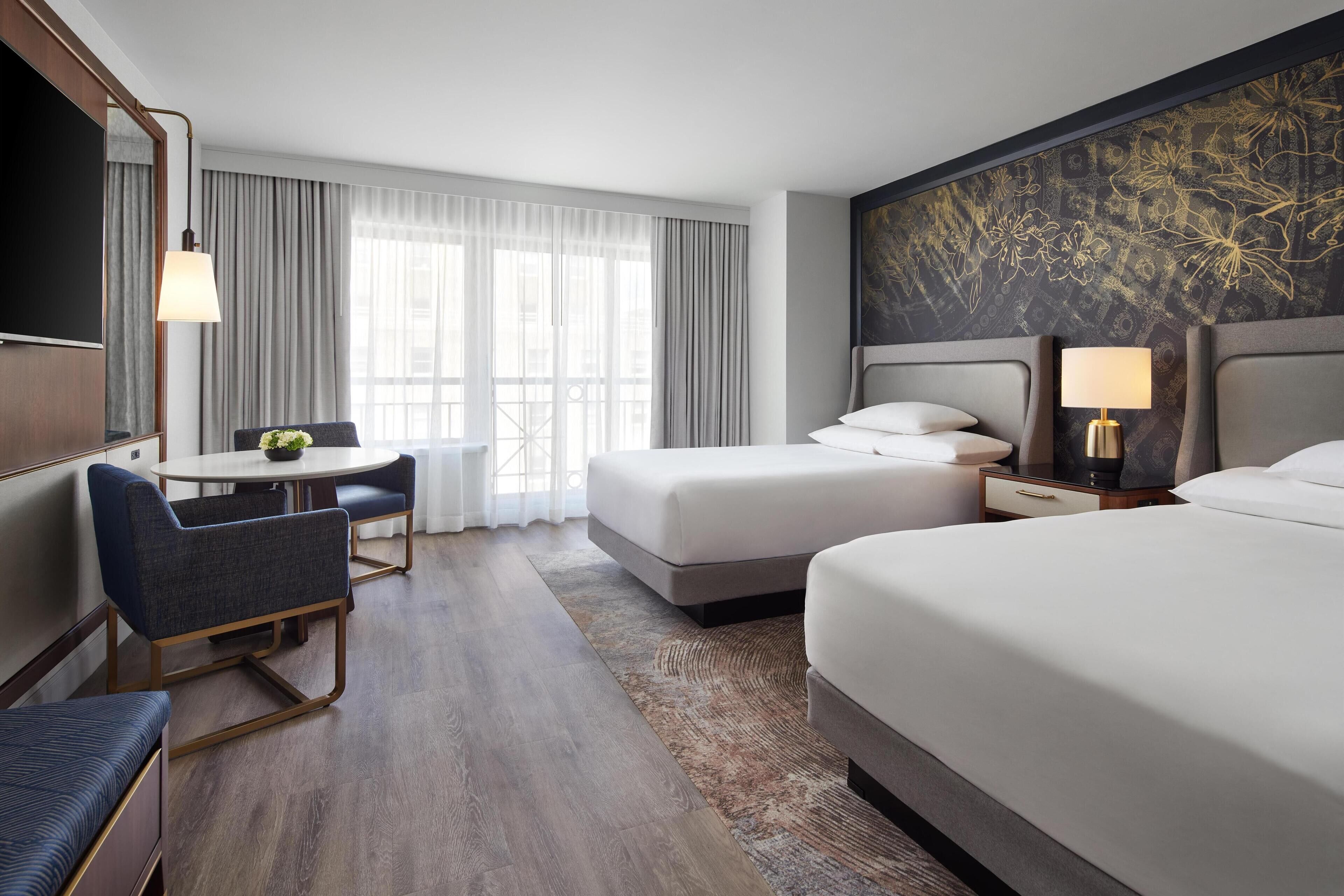 Habitación de hotel con una cama grande, un escritorio con silla, televisión y ventana con cortinas.