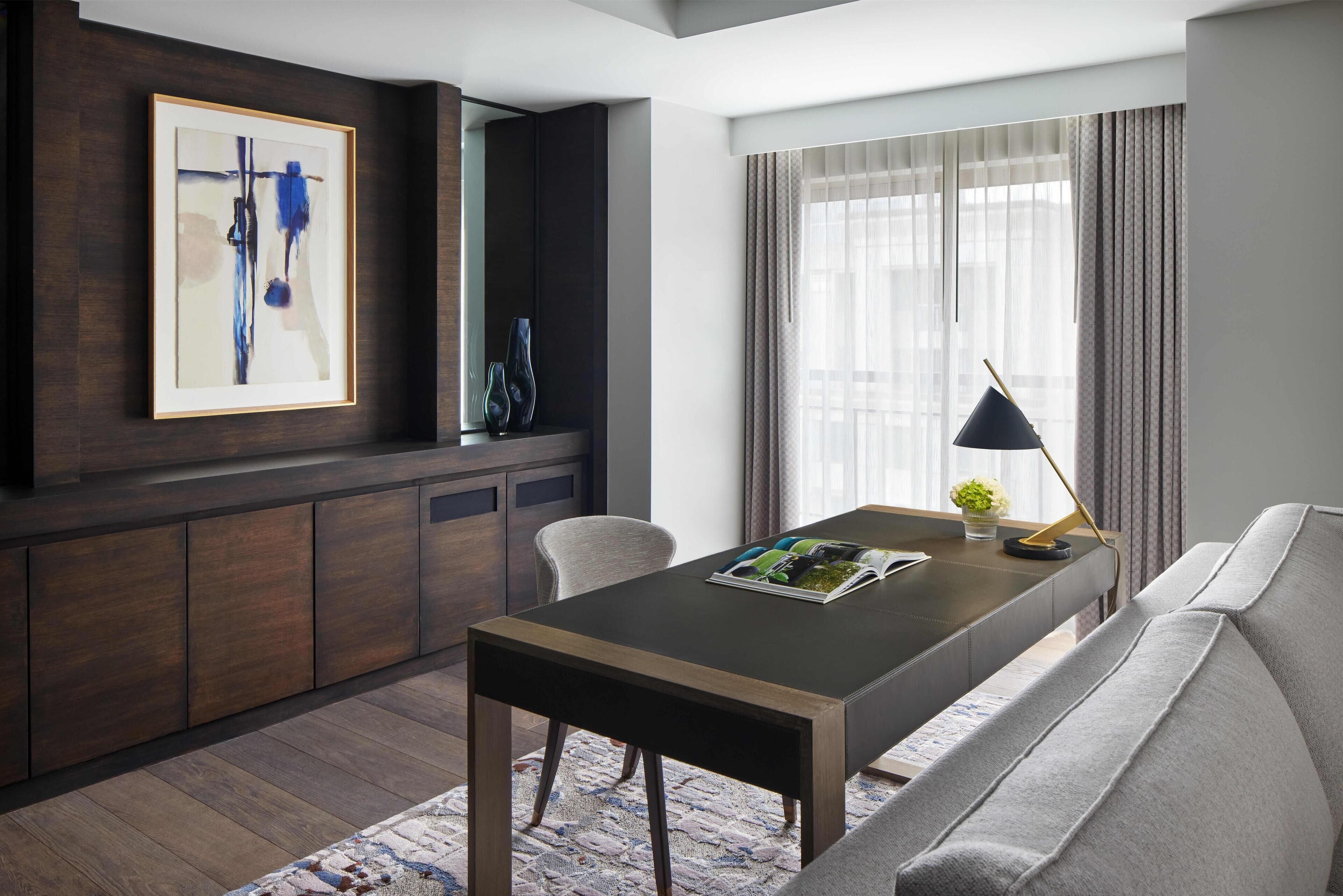 Una sala de estar moderna con un mueble de madera oscura, un cuadro abstracto enmarcado, un sofá, una mesa de centro y una ventana con cortinas.