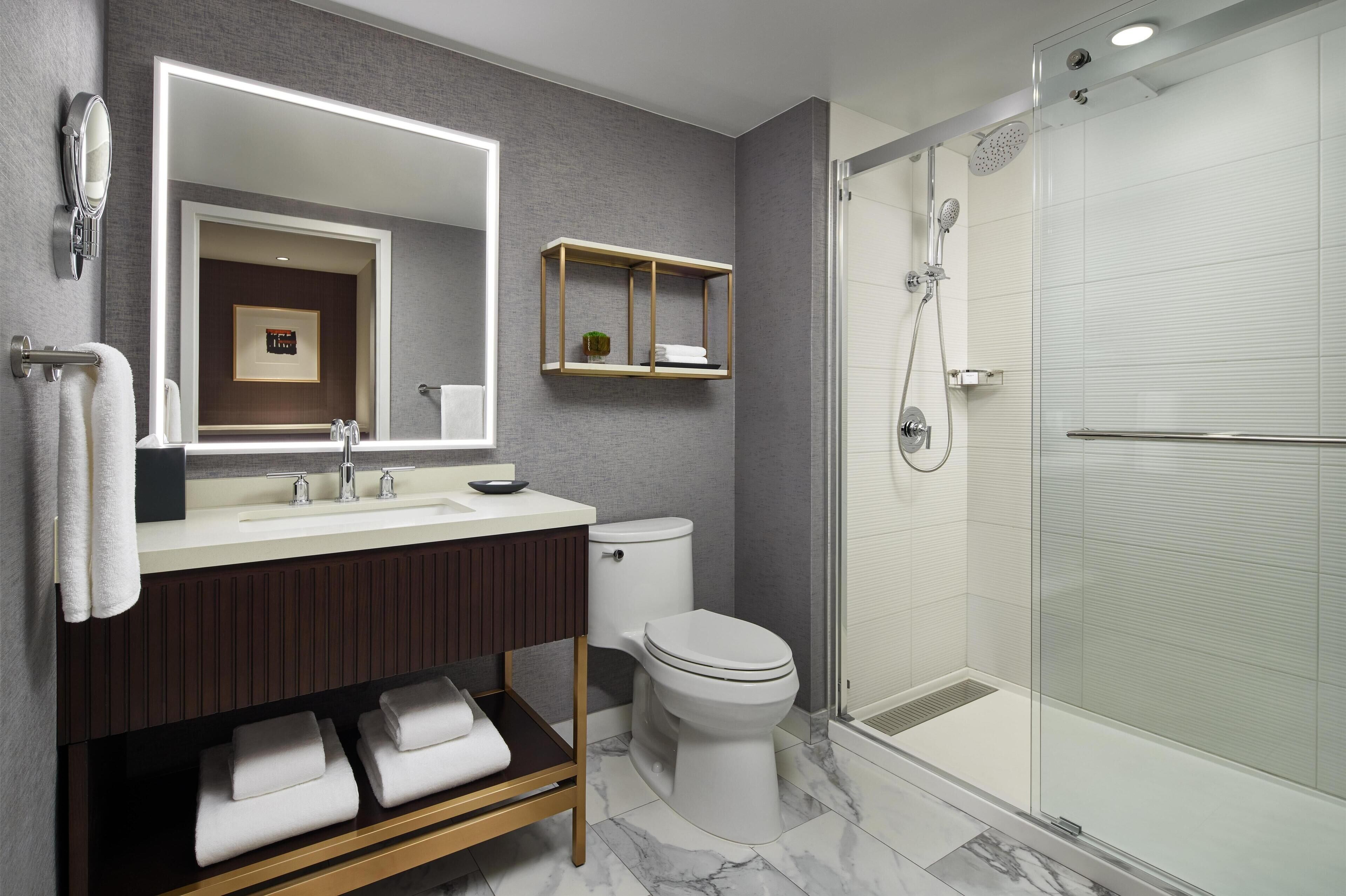 A modern bathroom with a large mirror, a vanity with a sink, a toilet, and a glass-enclosed shower area.