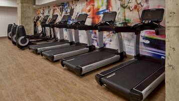 A row of treadmills in a gym with a colorful abstract mural on the wall.