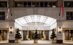 Indgangen til Grand Hyatt hotellet, med en markant buet glasmarkise, store plantede træer og flag.