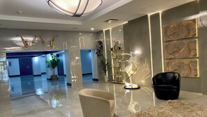 A modern lobby with a reflective floor, a central seating area, and a large abstract wall art piece.