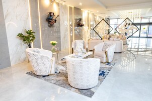 Un vestíbulo moderno con paredes de mármol, una zona de estar con sillones blancos y un amplio ventanal que proporciona luz natural.