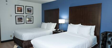 A hotel room with two beds, a desk, a chair, and a wall with framed pictures.