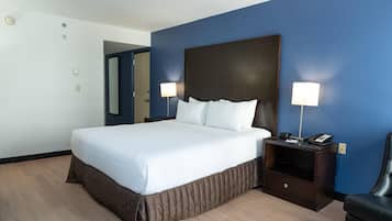 A hotel room with a large bed, two bedside lamps, a nightstand with a phone, and a door leading to another room.