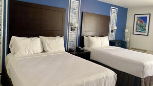 A hotel room with two beds, each with white linens and a dark headboard. There is a nightstand with a lamp and a telephone on one side.
