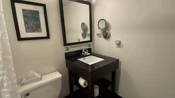 Une salle de bain avec des toilettes blanches, un lavabo noir avec un miroir au-dessus, et un tableau encadré accroché au mur.