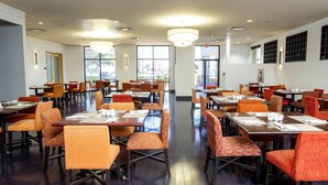 A spacious dining area with multiple tables and chairs, large windows, and a clean, modern design.