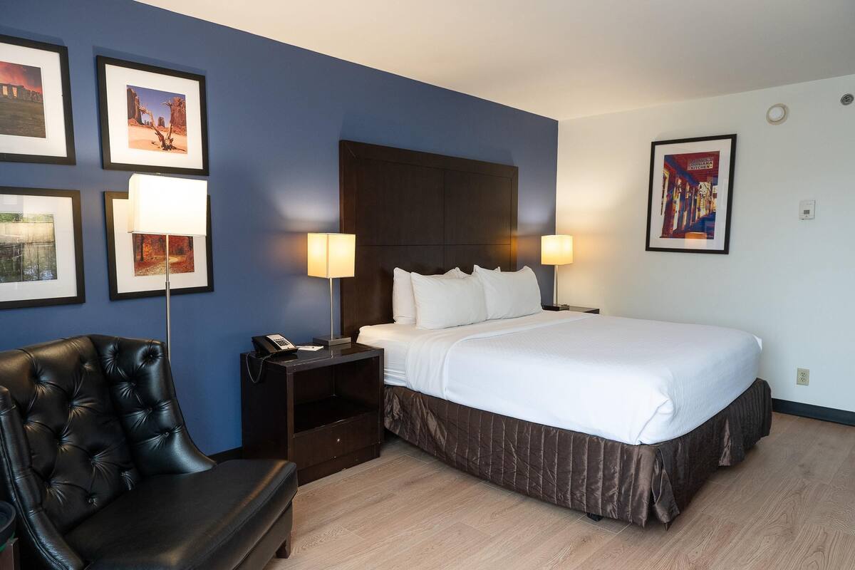 Une chambre d’hôtel avec un lit, une chaise, une table de chevet et des lampes fixées au mur.