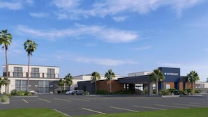 A modern hotel with a parking lot, palm trees, and a clear sky.