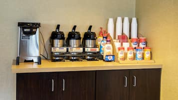 Una estación de café con una máquina de café, varios dispensadores de café y una selección de botellas de leche para café.