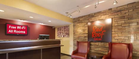 A hotel reception area with a Red Roof Inn sign, a free Wi-Fi sign, and leather chairs.
