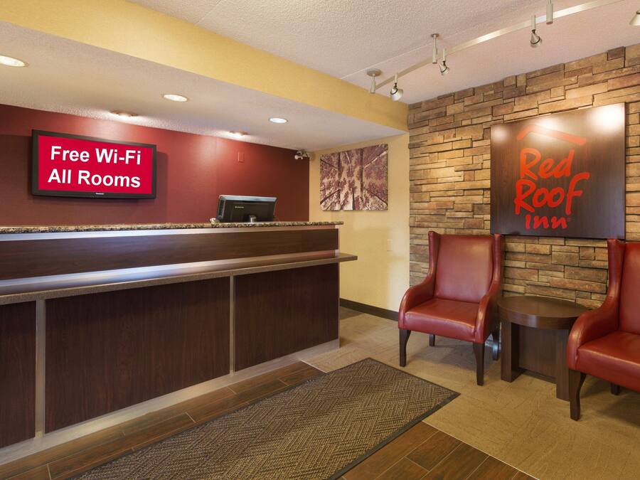 A hotel reception area with a Red Roof Inn sign, a free Wi-Fi sign, and leather chairs.