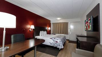 Une chambre d’hôtel avec un lit, un bureau, une chaise, une télévision et une porte.