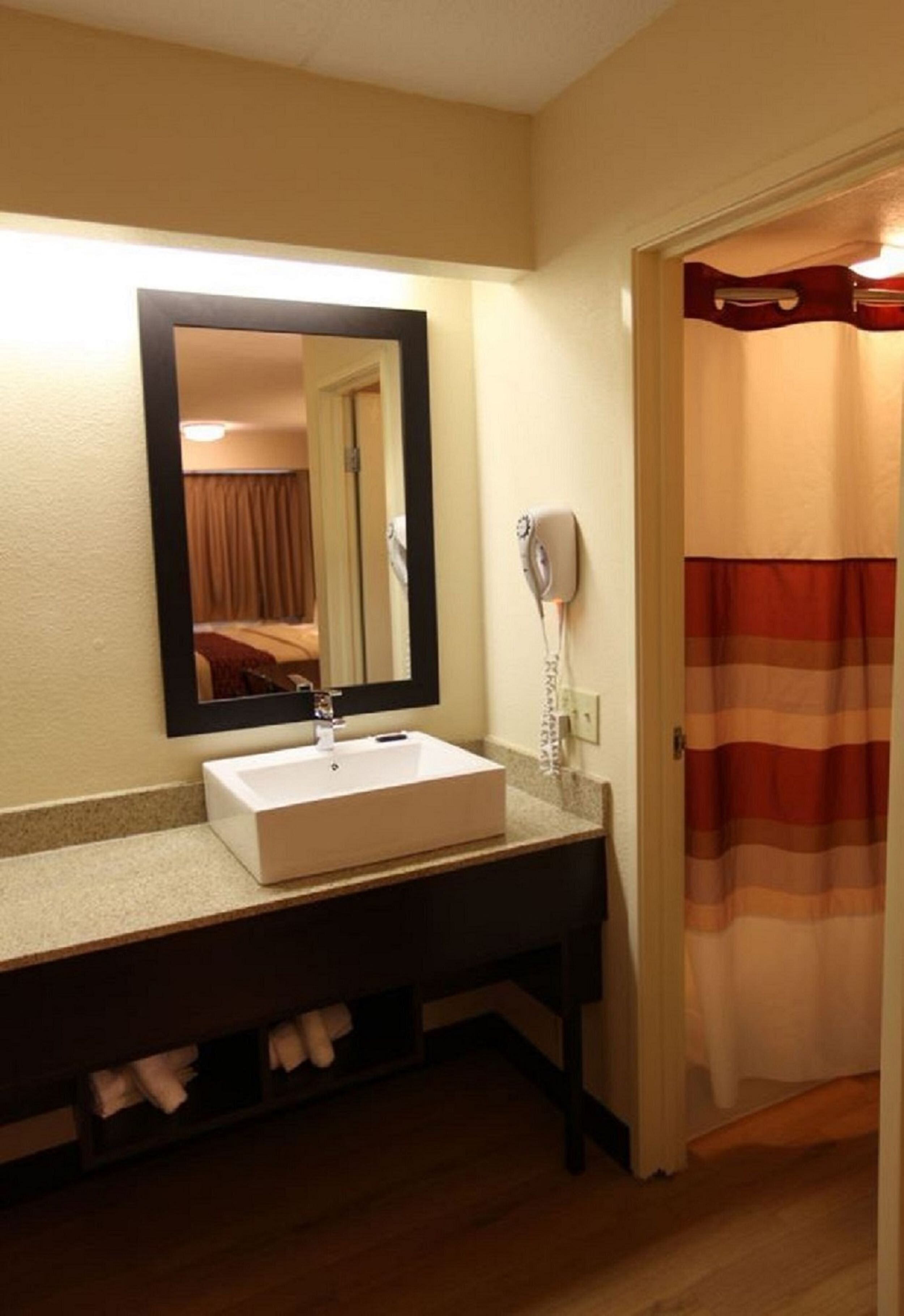 Une salle de bain avec un lavabo blanc, un miroir, un sèche-cheveux et un rideau de douche.