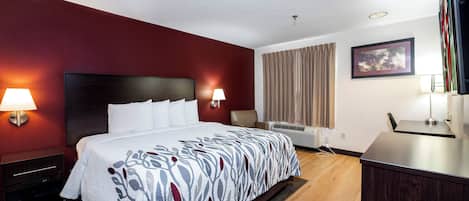 A hotel room with a bed, bedside lamps, an air conditioning unit, a desk, and a framed picture on the wall.