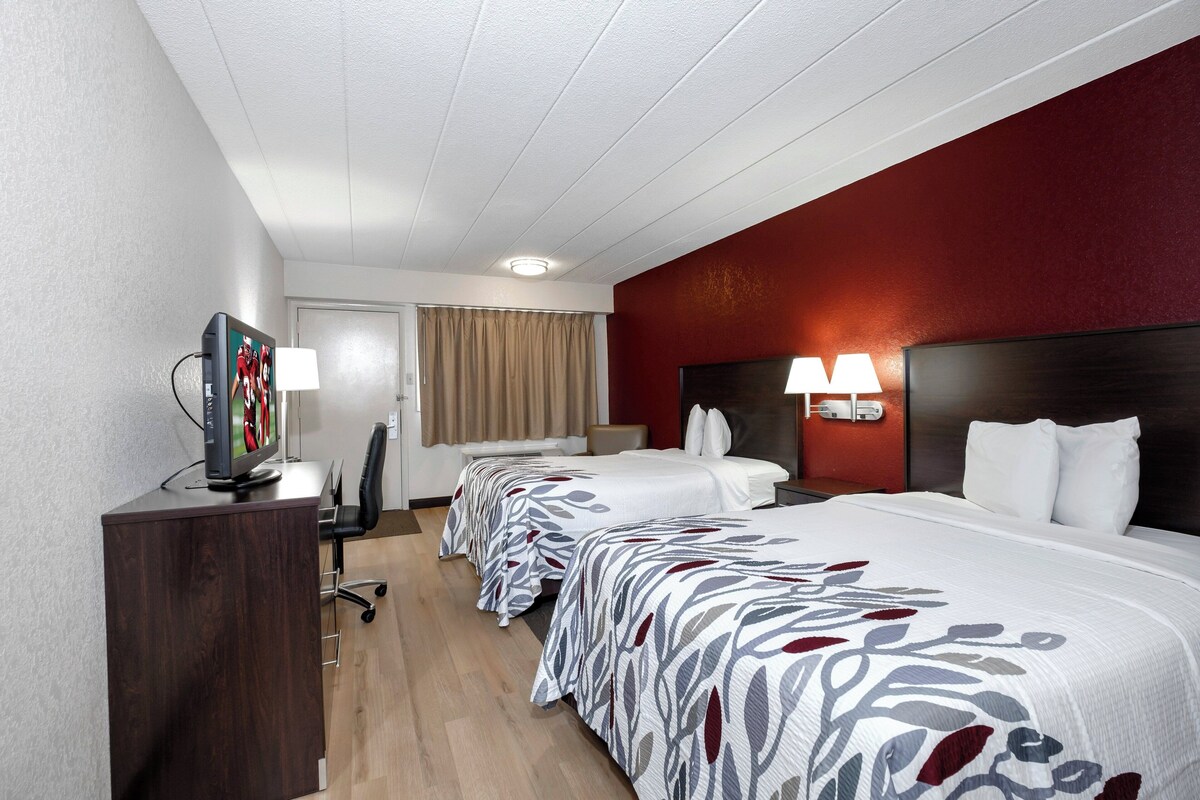 A hotel room with a bed, a desk with a computer, a TV, and a lamp.
