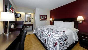 A hotel room with a bed, a desk, a chair, a lamp, a mirror, and a picture on the wall.